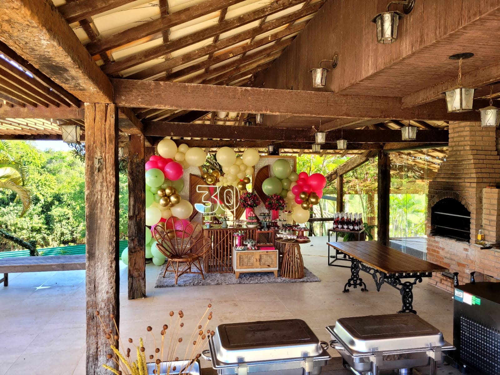 Espaço coberto montado para festa, com decoração, buffet e churrasqueira de tijolos